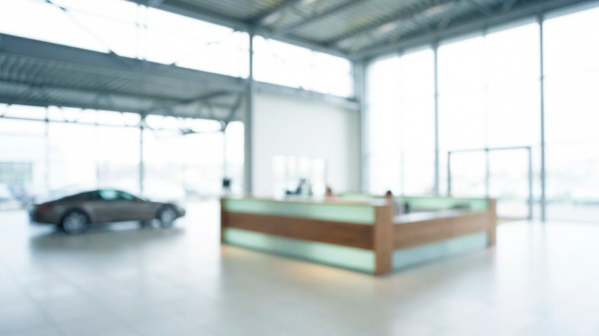 Autohaus, unscharf: eine helle Halle mit Stahldach, in der Mitte ein Empfangstresen mit Holzrahmen und grün leuchtenden Glasfeldern, links ein Fahrzeug