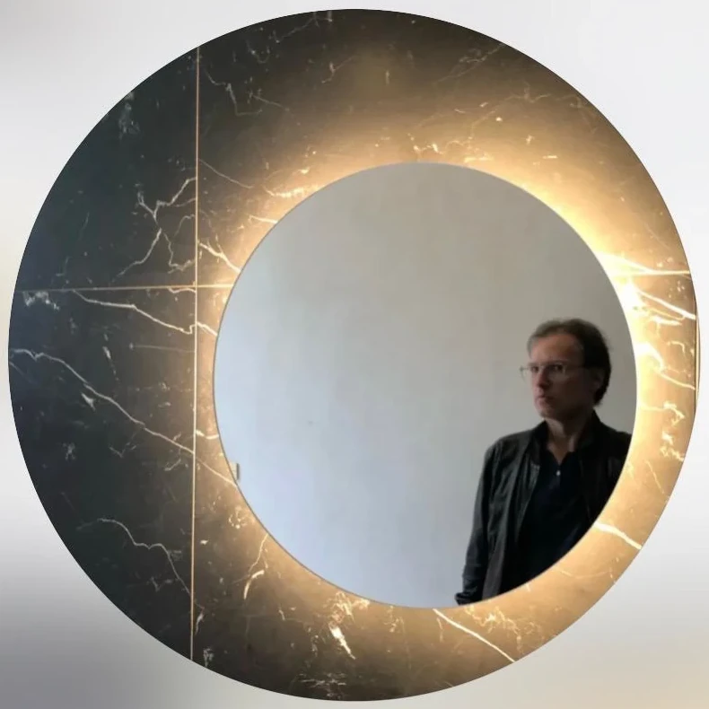 Thomas Stempel, gespiegelt in einem runden Spiegel mit schwarzem Marmorrahmen und warmem Lichtkranz